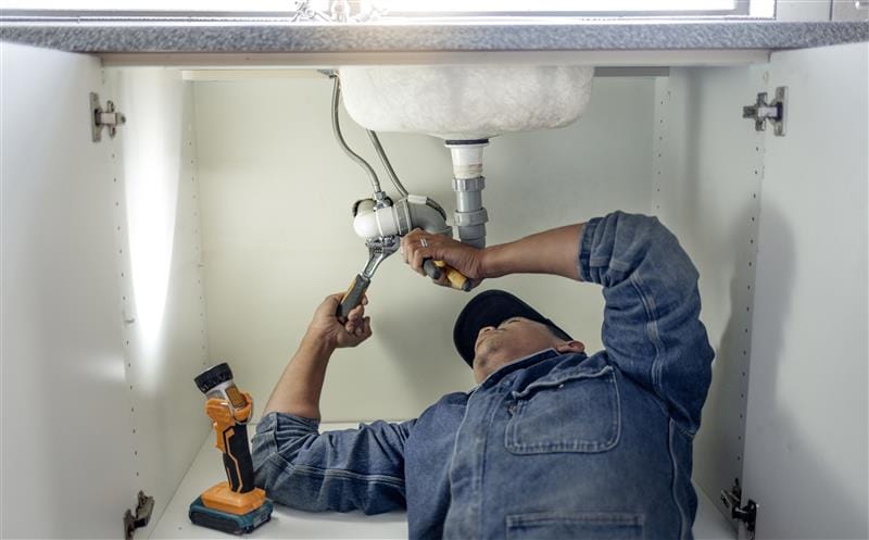 Plumber repairing pipes beneath a bathroom sink in San Jacinto