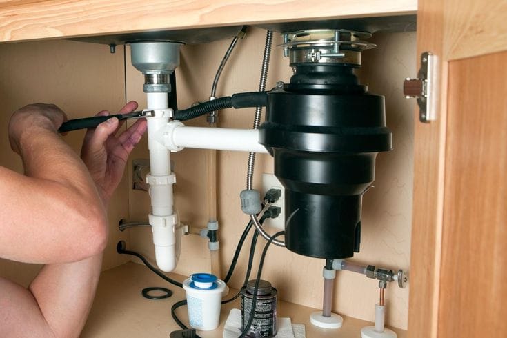 Plumber installing a garbage disposal beneath a kitchen sink in San Jacinto