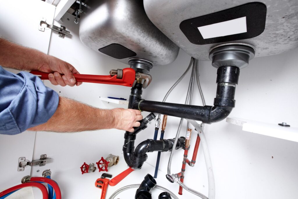 Plumber repairing drain pipes beneath a kitchen sink in San Jacinto
